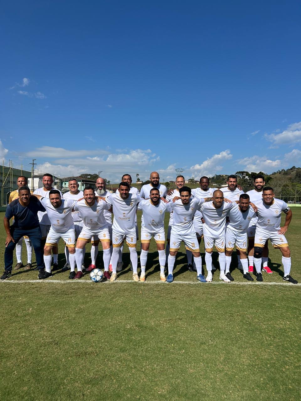 Elenco do Real Amigos FC posado em campo com o uniforme branco e dourado